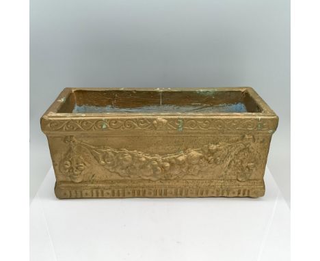 A gold-colored planter adorned with intricate grapevines, featuring a captivating man's face along with abstract artwork on i