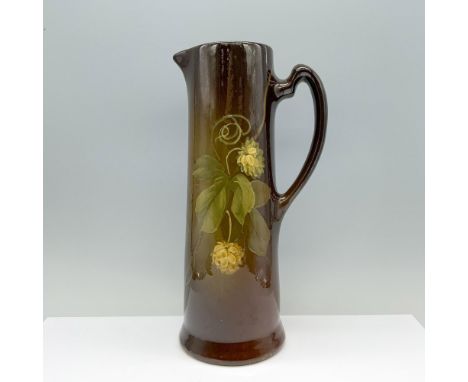 A beautifully glazed brown pitcher adorned with elegant white peonies and delicate foliage. Marked Owens. Marked 1015. Dimens