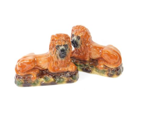 A mid 19thC pair of Bowness pottery figures of lions, modelled in recumbent pose, with glass eyes, on a naturalistic oval bas