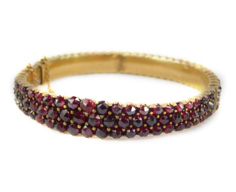 A late 20thC garnet bangle, with three row design of garnets, in yellow metal casing, marked 9ct to clasp, with safety chain,