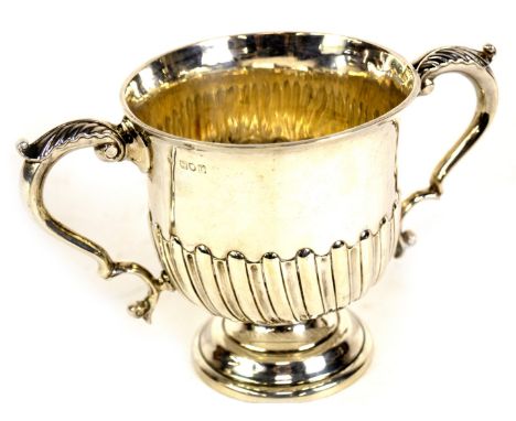 A late Victorian silver two handled loving cup, of semi whorl fluted urnular design, the scroll handles with acanthus caps an