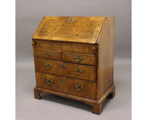 A GEORGE I WALNUT VENEERED BUREAU. An early 18th century walnut veneered bureau with a sloping fall with broad crossbanding, 