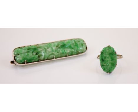 An Art Deco style jade ring, the claw set carved oval panel ring decorated as flowers, 2cm long, mounted in white metal marke