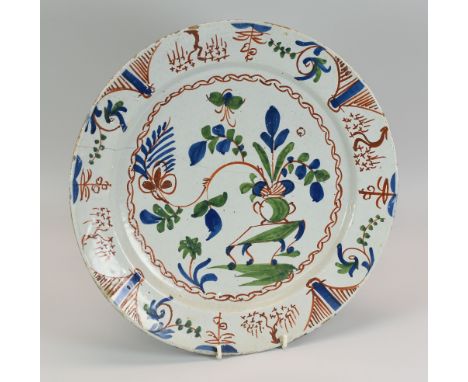 A DELFT TIN-GLAZED POTTERY CHARGER primitively painted in blue, green and red with a jardiniere on a table and within a chain