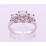 An 18 K white gold three-stone diamond ring. The central stone spreading to approximately 1 carat.