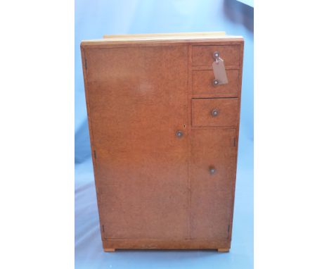 An Art Deco birdseye maple cabinet with large cupboard door beside three drawers and one small door raised on block feet. H-1