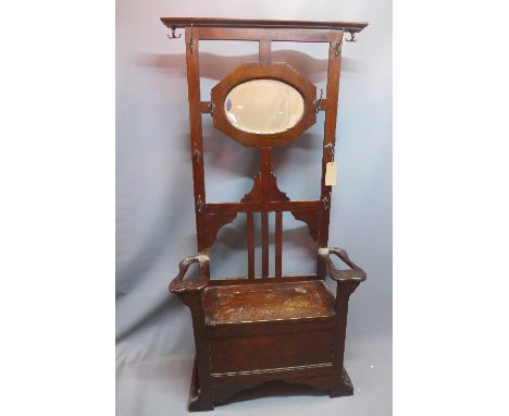 An early 20th Century oak hall stand with oval bevelled mirror back plate above seat with hinged lid flanked by stick stands.