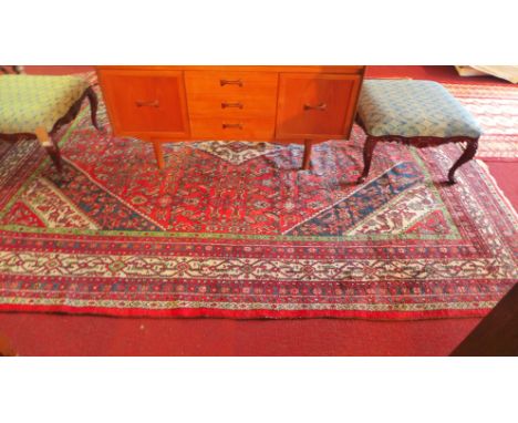 A large Persian Hamadan carpet with geometric diamond medallion on a red ground contained by repeating geometric borders. 350
