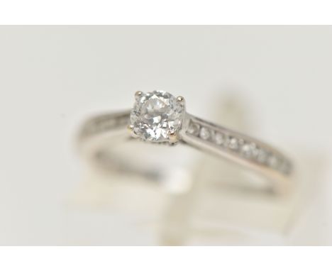 A 'THE FOREVER DIAMOND' DIAMOND RING, a round brilliant cut diamond four prong set in white gold, leading on to channel set d
