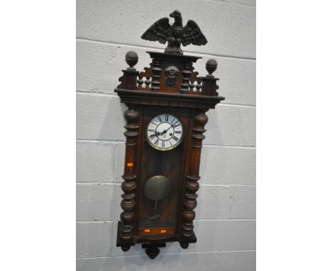 A LATE 19TH CENTURY WALNUT CASED VIENNA WALL CLOCK, with an eagle pediment, above a human mask, flanked by two finials, the g