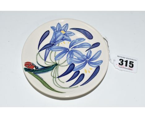 A MOORCROFT POTTERY TRINKET DISH, in 'Fly Away Home' pattern, tube lined with a ladybird climbing the stem of a blue flower o