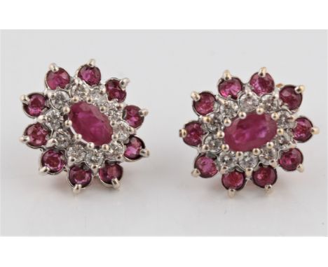 A pair of ruby and diamond tiered cluster earrings, set with a central oval cut ruby, surrounded by ten round brilliant cut d