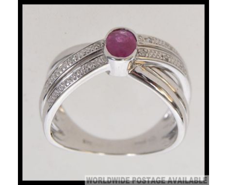 A modern 9ct white  gold ( stamped 375 ) dress ring of cross over style, having a single ruby coloured cut and polished stone