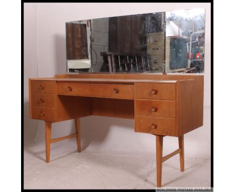 A retro 1970's Ernest Gomme for G-Plan light oak dressing table raised on tapered legs with a series of drawers having triple