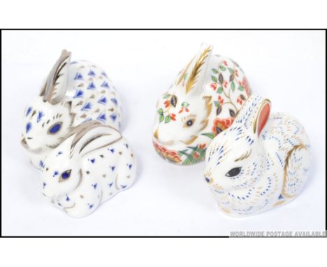 Four Crown Derby paperweights Bunny with gold button , Meadow Rabbit silver button and two other rabbits of similar form .