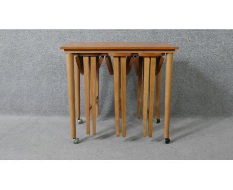 A vintage light teak nest of tables on beech supports fitted with three slide out drop flap occasional tables. H.56 W.63 D.42