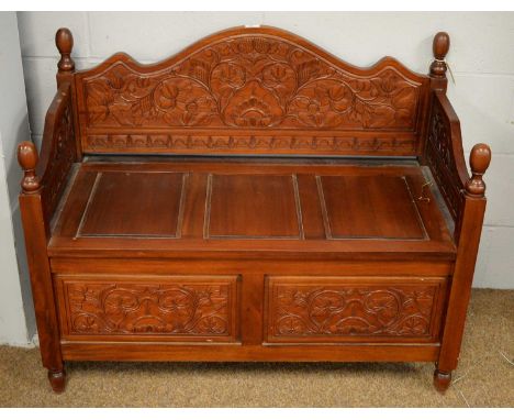 A 20th Century stained monks bench, with shaped foliate sides and turned finials, above a hinged seat and raised on foliate c