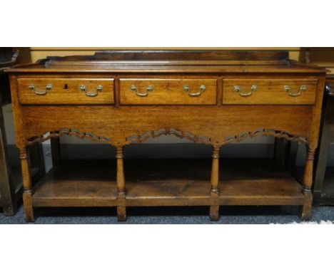 An oak dresser base with open plank shelf, pierced apron to four baluster supports and with three drawers, circa 1840, 57.5in