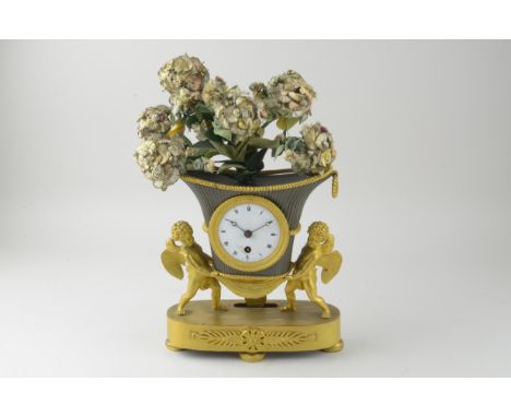 A small French Mantel Clock of urn shape with circular white enamel dial, supported by two cherub gilt figures on a decorativ