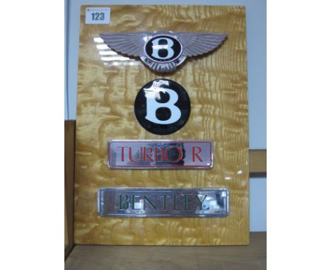 Four Bentley Badges, nicely presented on a wooden mount, winged Bonnet Badge B, Black B Wheel Centre Badge, Turbo R and Bentl