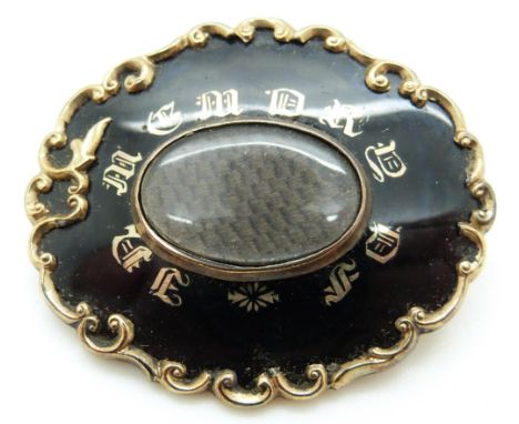 A Victorian mourning brooch set with black enamel with gold writing "In Memory of" and with a glass compartment to the centre