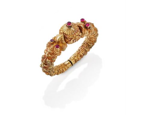 AN EARLY 20TH CENTURY INDIAN MARAKA HEAD BANGLE   The gold bangle with chased Maraka heads, with red foiled cabochon stone ey