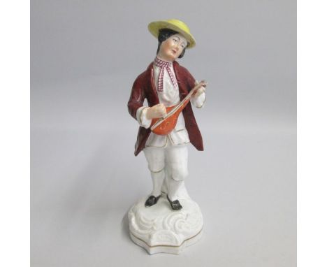 A Staffordshire figure of a male musician playing lyre, standing on a scrolled base, dressed in a brown coat and yellow hat.
