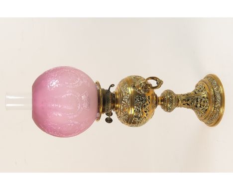 Victorian brass pedestal oil lamp, having a globular etched cranberry glass shade over a metal tank housed within a pierced R