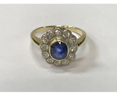 A gold mounted sapphire and diamond cluster ring, the central oval cut stone, approx 0.5 carat, within a band of 12 diamonds,