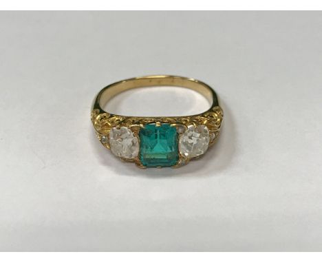 An 18 carat gold ladies dress ring set with central rectangular but emerald, approx 1 carat, flanked by two diamonds, approx 