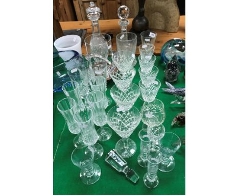 A collection of glassware to include a Robert Welsh hurricane lamp, two cut glass decanters, various Waterford wine glasses a