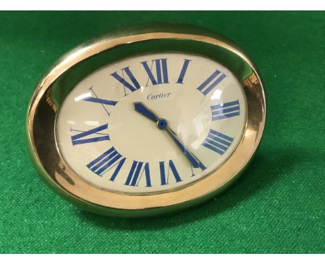 A Cartier travel clock of oval curved form, the enamel dial set with blue Arabic numerals and blue painted hands inscribed "C