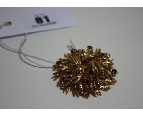 A 9ct gold and ruby brooch pendant in the form of an abstract textured and stylized leaf cluster, sprinkled with nine small r