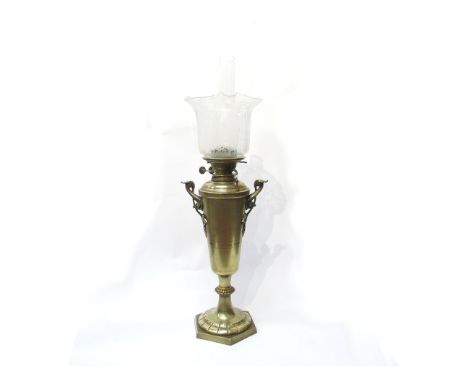 A brass oil lamp, urn form base with twin scroll handles set on a hexagonal base with clear shade etched with scrolls