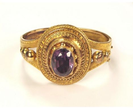 VICTORIAN BANGLE.A Victorian yellow metal bangle, the front set a large dark amethyst in an Etruscan Revival setting, the sho