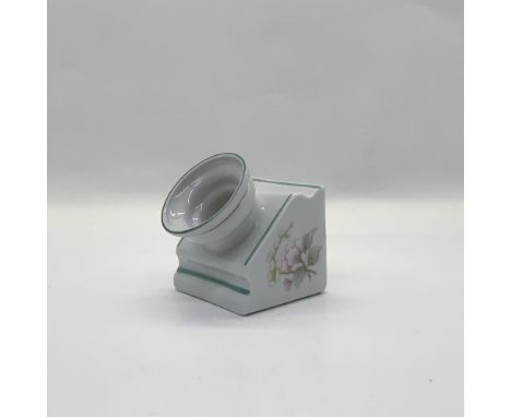 A white porcelain angled vessel with inkwell insert and pen rests, decorated with pink and yellow flowers. This item has its 