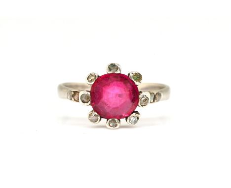 A SYNTHETIC RUBY AND DIAMOND RINGThe central oval cut synthetic ruby, with a rose cut diamond surround, in white metal, gross