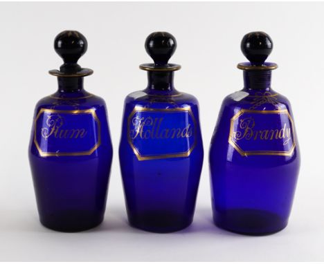 THREE BLUE GLASS SPIRIT DECANTERS AND STOPPERSEarly 19th centuryOf barrel form, with gilt octagonal labels for `Hollands', `B