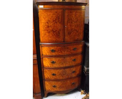 A bow fronted figured walnut cupboard on chest, a pair of cupboard doors enclosing a single shelf above four long drawers on 