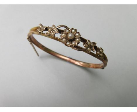 A seed pearl hinged bangle, designed to the front as a flowerhead with trailing leaves all set with seed pearls (one lacking)