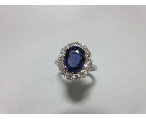 A sapphire and diamond cluster ring, the oval cut royal blue sapphire in a border of round brilliant cut diamonds, claw set t