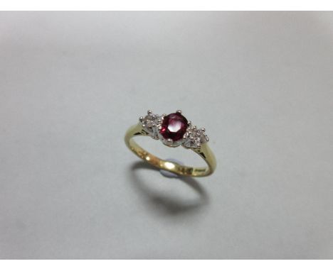 An 18ct gold ruby and diamond ring, the oval cut ruby between two round brilliant cut diamonds claw set in white gold to a pl