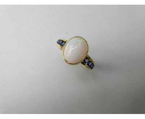 An opal and sapphire ring, the central collet set oval cabochon opal between shoulders of channel set round cut sapphires, to