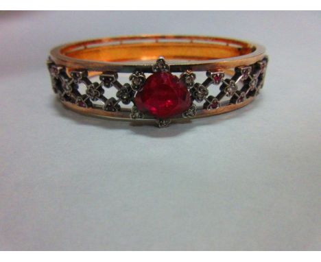 A ruby and diamond hinged bangle, set to the front with a trellis of trefoils and quatrefoils each with a small rose cut diam