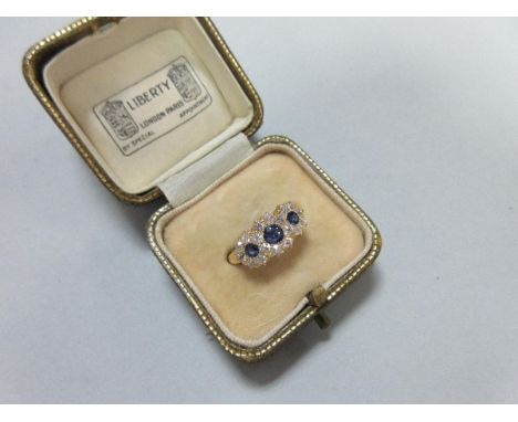 An Edwardian sapphire and diamond ring in period Liberty case, designed as a triple flowerhead with three round cut mid-blue 