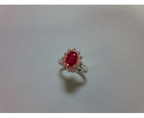 A ruby and diamond cluster ring, the oval cut ruby claw set in a border of twelve round brilliant cut diamonds to a plain pol