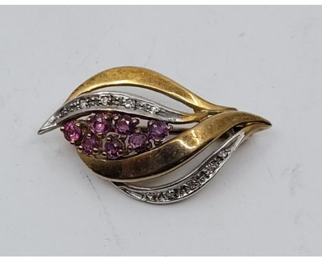 A bi-colour 9ct. gold, ruby and diamond set brooch, claw set seven mixed round cut rubies and pave set diamonds to either sid