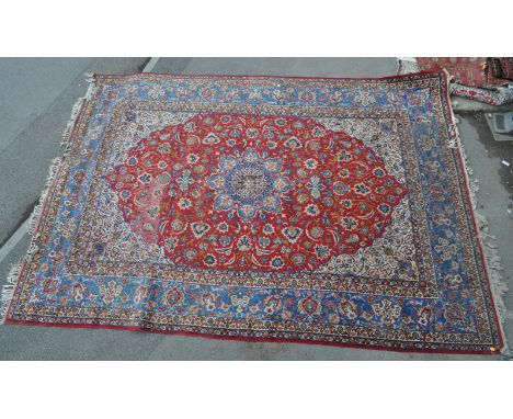 A large early 20th century Persian Kashan rug carpet having a central blue and whiter medallion upon a red ground with blue b