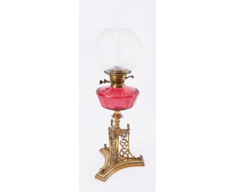 A Victorian Gothic style oil lamp, with ornate brass base, cranberry glass reservoir and glass etched shade on ornate base.