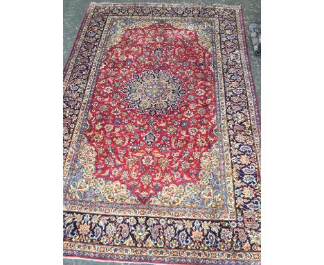 PERSIAN HAND KNOTTED WOOL CARPET, with a central roundel of floral designs, surrounded by floral motifs on a red ground, and 